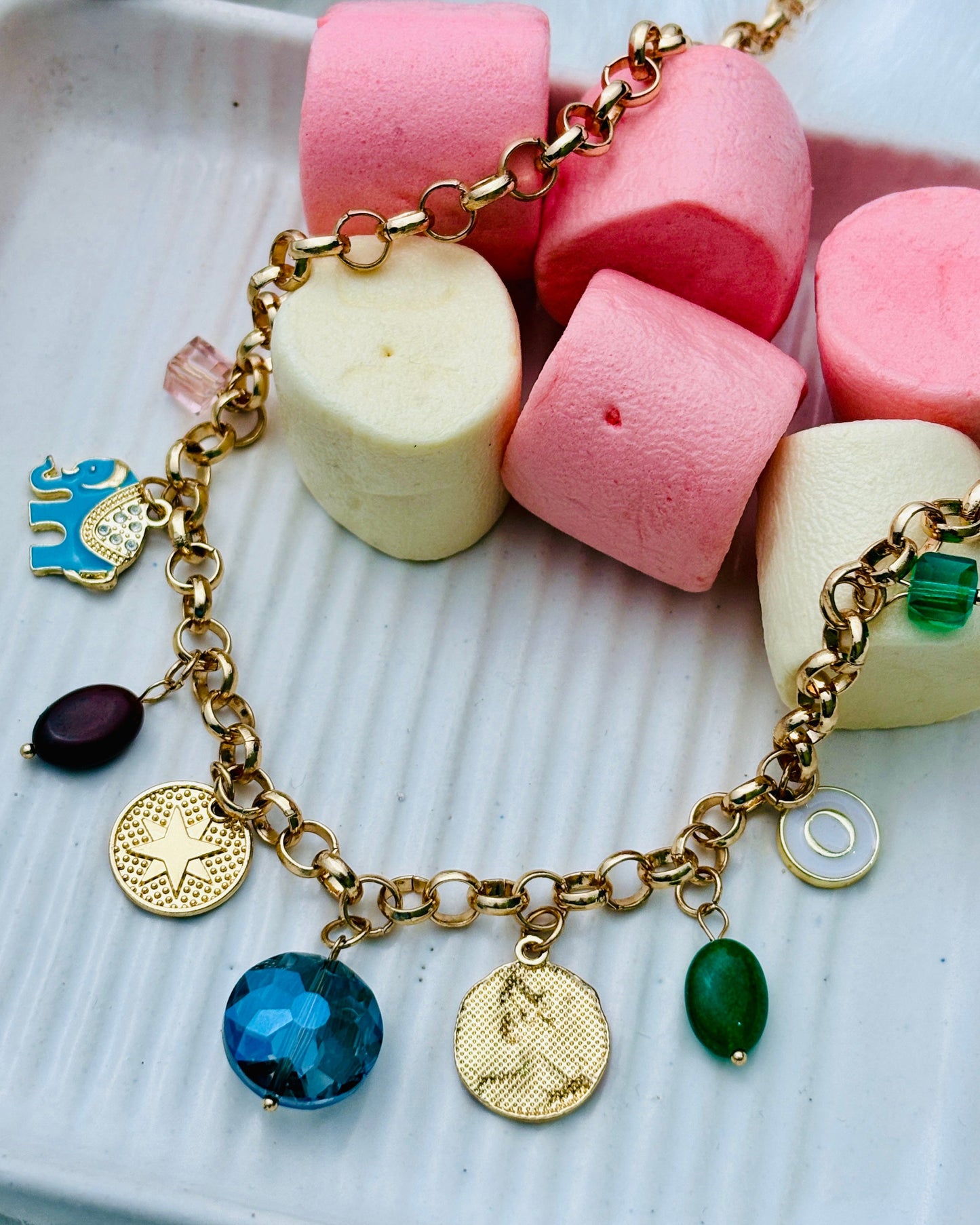 Gold bracelet with charms on a plate of colorful marshmallows